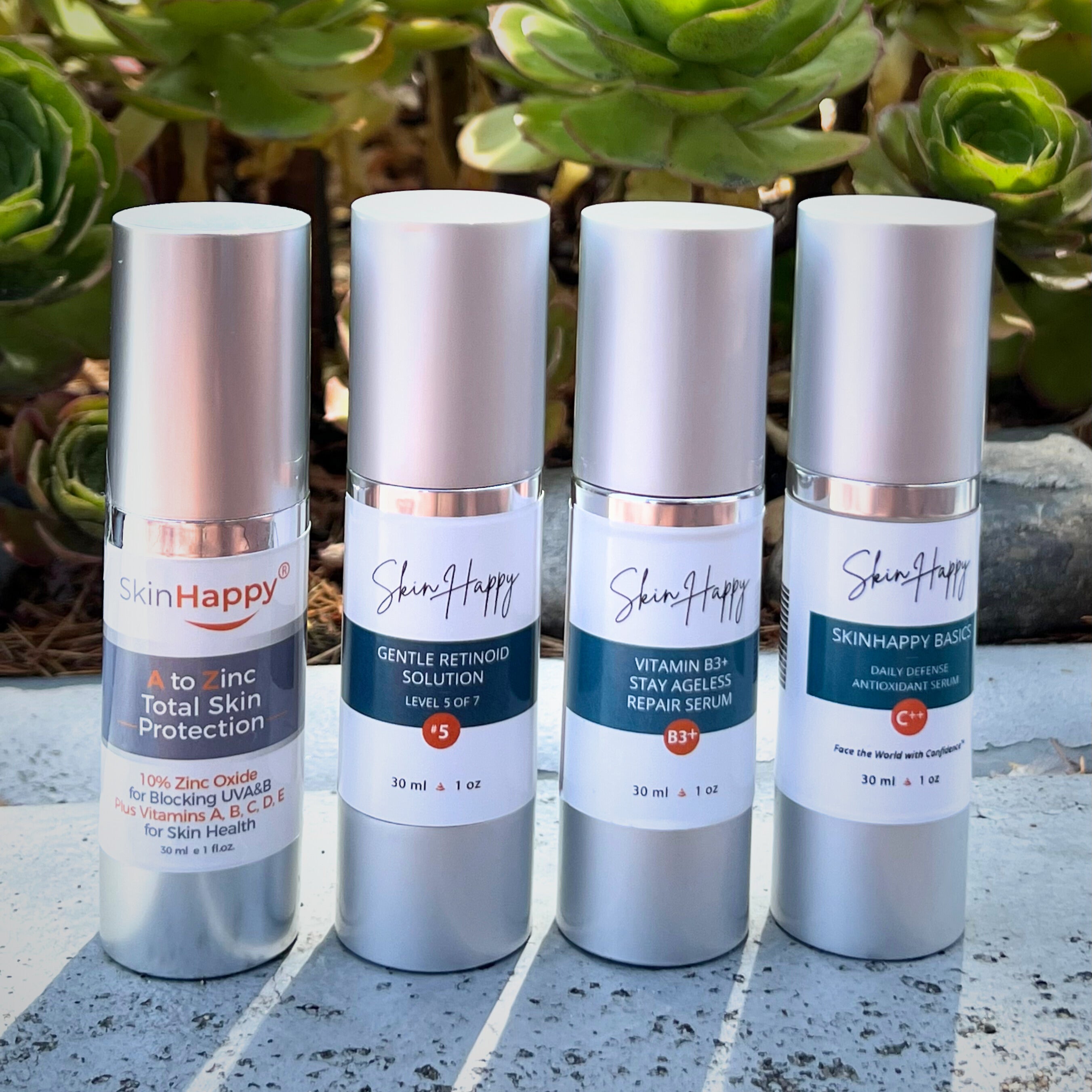 Four SkinHappy skincare product bottles on a stone surface with green plants in the background.
