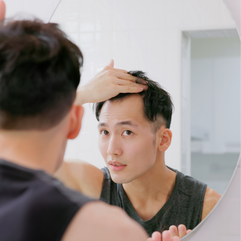 Man examining his hair in a bathroom mirror