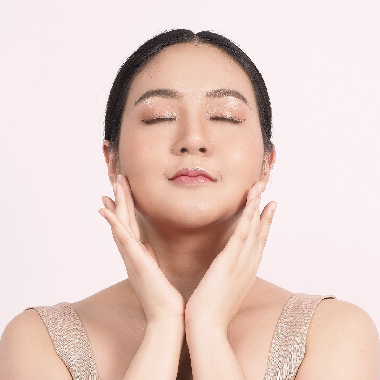 Smiling woman with hands on face against a light pink background