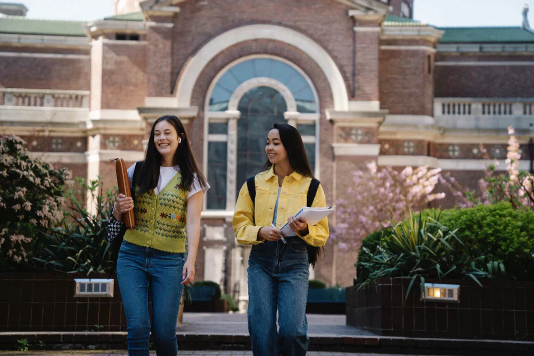 Two people walk carrying books on a school campus.