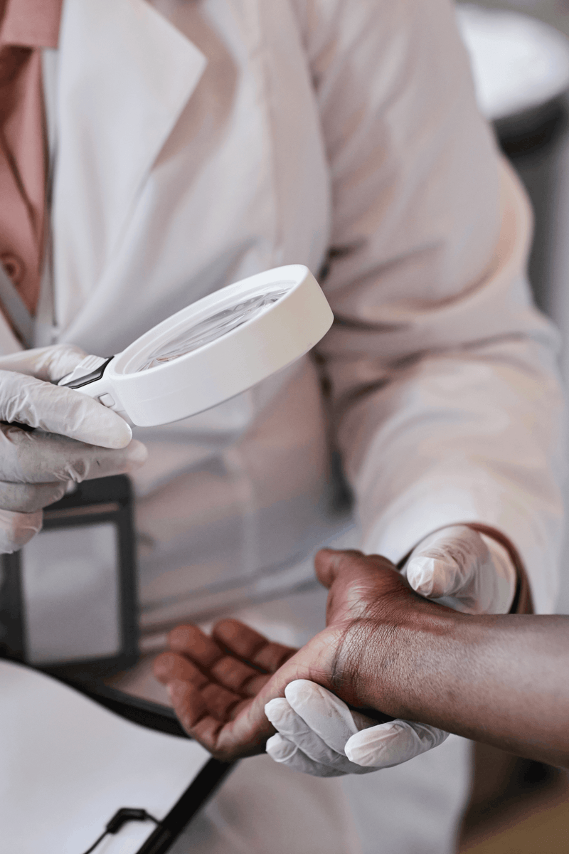 A doctor examines a patient's hand under a magnifying glass.