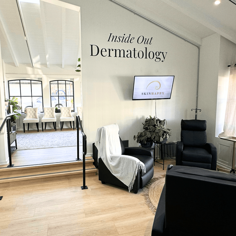 An interior view of the SkinHappy Dermatology clinic, with comforting white walls and cozy chairs. A sign on the wall says "Inside Out Dermatology". 