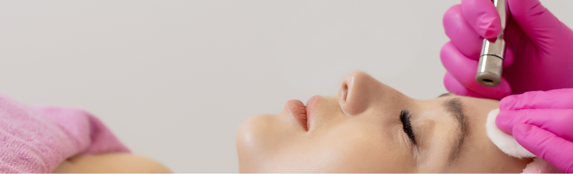 Facial treatment with a handheld device and gloved hands on a neutral background