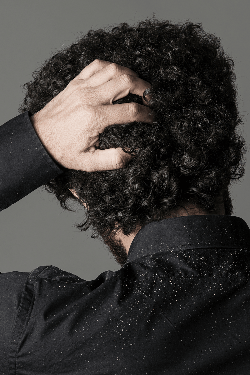 A person scratching their head with dandruff flakes on a black shirt.