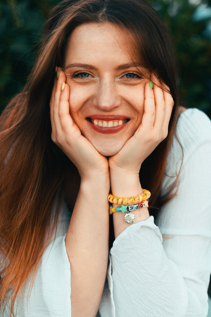 A smiling woman holding her face outdoors, wearing a bracelet that spells Hope.